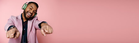 Young African American man joyfully points while wearing headphones against a vibrant pink backdrop.