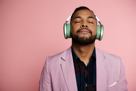 A young African American man listening to music through headphones on a pink background.の写真素材