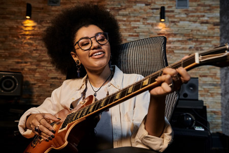 A woman with glasses strums a guitar in a recording studio during a music band rehearsal.