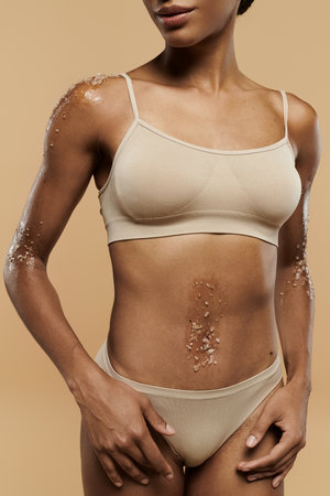 A captivating African American woman in lingerie radiates confidence and beauty against a soft beige backdrop.の写真素材
