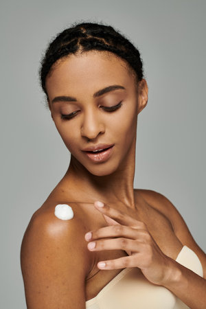 A beautiful young African American woman in a strapless top applying a thick layer of cream to her face on a grey background.の写真素材
