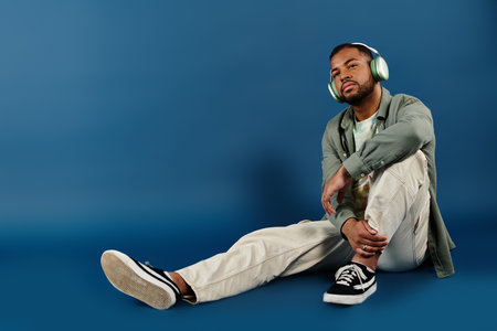 Stylish African American man sitting on floor, lost in music with headphones on.の写真素材
