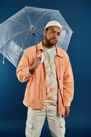A stylish African American man holding a clear umbrella over his head against a vibrant backdrop.の写真素材