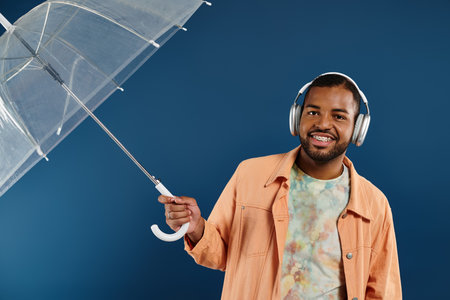 Stylish African American man in headphones holding an umbrella under vibrant backdrop.の写真素材