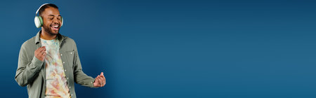 Stylish African American man with headphones standing in front of vibrant blue backdrop.の写真素材