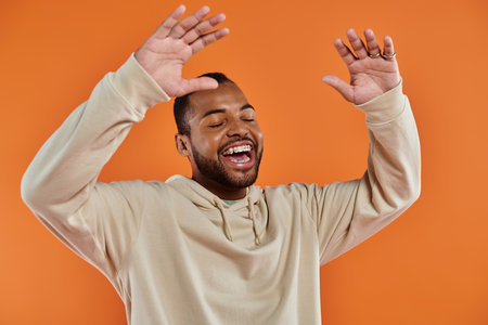 A stylish African American man with hands raised in delight on a vibrant backdrop.の写真素材