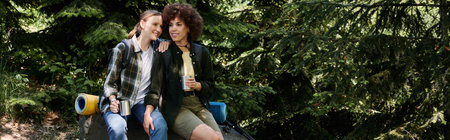 A young lesbian couple enjoys a hike in the woods, taking a break to share a drink and laugh...