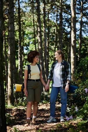 A young lesbian couple hikes through a forest, hand in hand, enjoying a sunny day.の写真素材