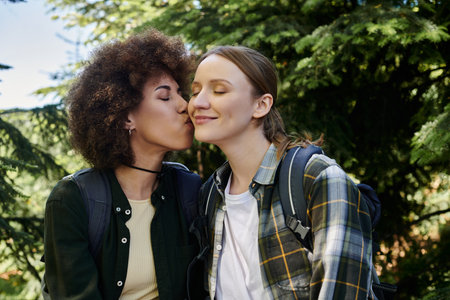 A young lesbian couple enjoys a hike in the woods, sharing a tender moment.