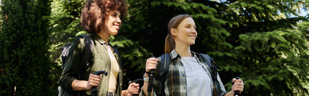 Two young women, dressed in casual clothing, hike through a forest, enjoying the outdoors together.の写真素材