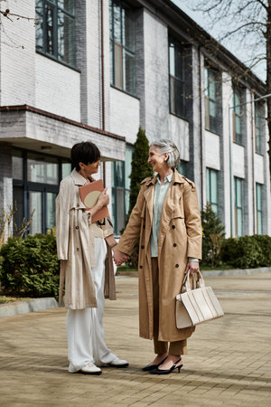 Two women, a mature beautiful lesbian couple, standing hand in hand in front of a building.の写真素材