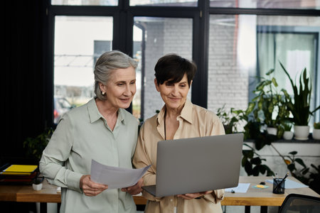 Two women collaborate on a project using a laptop in an office setting.の写真素材
