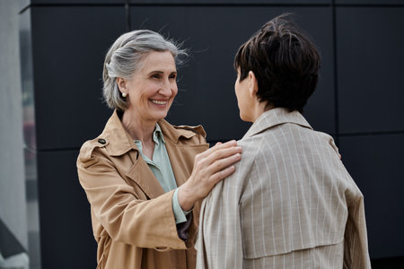 Mature, beautiful lesbian couple walking to office in trench coats.