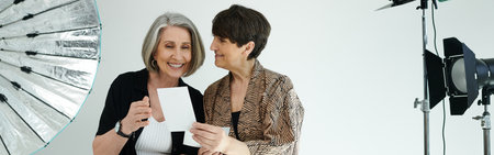 Middle-aged lesbian couple looking at printed photo in a studio, behind the shot