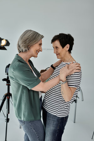 A middle-aged lesbian couple stands confidently side by side in a professional modern photo studio.