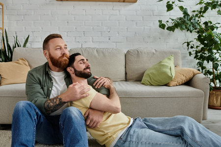 Two bearded men relax on a couch, enjoying each others company in a warm living room.の写真素材