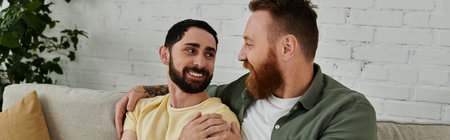 A couple of men with beards sit comfortably on top of a couch, enjoying quality time together in a living room.の写真素材