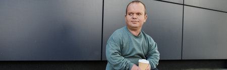 A man with inclusivity sits casually in front of a modern building, holding a cup of coffee.
