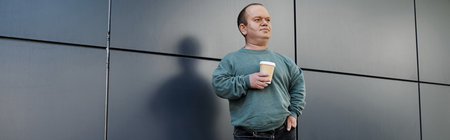 A man with inclusivity with a cup of coffee stands against a grey wall, contemplating his day.
