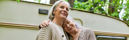 Two middle-aged women embrace, enjoying a peaceful moment in the green forest while camping near...