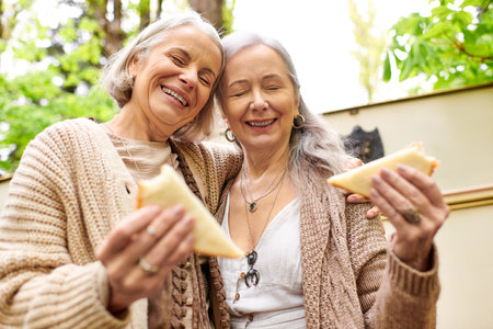 Two middle-aged women, a lesbian couple, are laughing and eating sandwiches while camping in a green forest.の写真素材