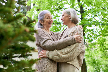 Two middle-aged women, a lesbian couple, embrace in a lush green forest setting while camping.