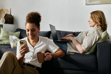 A lesbian couple relaxing at home, one using a phone and the other working on a laptop.の写真素材