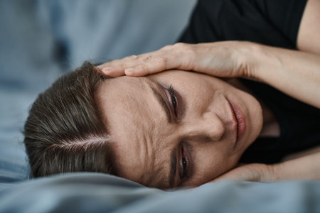 Middle-aged woman laying in bed with hand on head, deep in thought.の写真素材