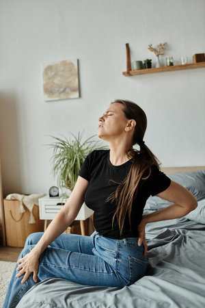 Woman sitting on bed, clutching her back in pain, struggling with depression.