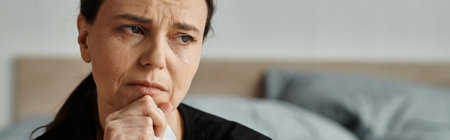 Woman sitting on bed, chin on hand, struggling with depression.の写真素材