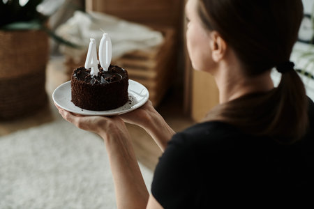 A middle-aged woman holding a birthday cake on a plate in a home setting.の写真素材
