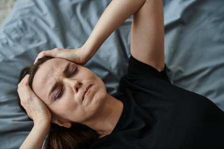 Middle-aged woman lying in bed, hands resting on head, contemplating.の写真素材