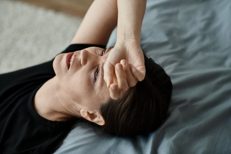 Middle-aged woman laying on bed with hand on head in a moment of introspection.の写真素材