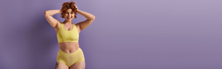 Curvy redhead woman in yellow bikini striking a pose against a vibrant purple backdrop.の写真素材