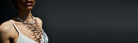 A stylish young woman in a white top gracefully poses with a necklace.の写真素材