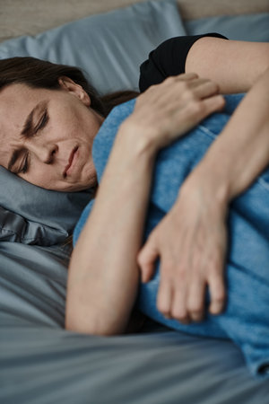 Middle-aged woman at home, laying in bed with hand on stomach.の写真素材