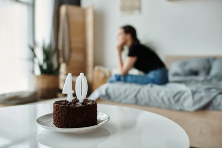A middle-aged woman sits alone on a bed with a cake, lost in thought.の写真素材