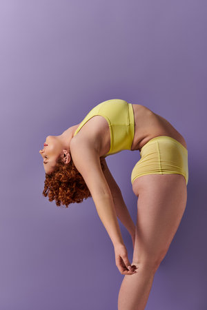 A young, curvy redhead woman in a yellow bikini performs yoga poses on a vibrant purple background.