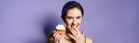 A pretty young woman with short blue hair in a silver party dress hides her face behind a delicious cupcake.の写真素材