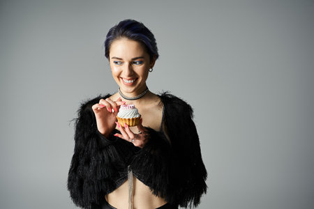 A pretty young woman with short dyed hair holds a colorful cupcake in her hands, admiring its intricate design.の写真素材