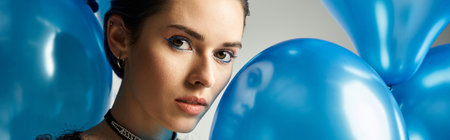 A stylish young woman with short dyed hair holds a collection of beautiful blue balloons in a studio setting.の写真素材