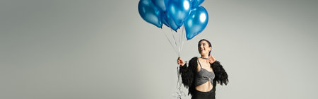 A woman with short dyed hair looks festive while holding a bunch of blue balloons in a studio setting.の写真素材