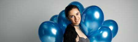 Young woman with short, dyed hair posing in front of a bunch of blue balloons in a studio setting.の写真素材