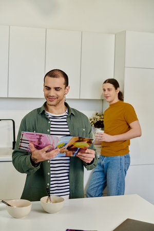 A young gay couple spends time together in their modern kitchen, one browsing a magazine while the...