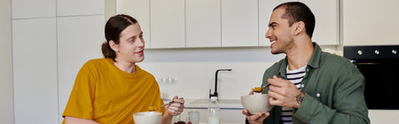 A young gay couple sits at a kitchen counter, enjoying a meal together in their modern apartment.