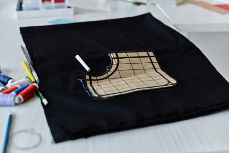 A close-up view of a black fabric laid flat on a table, a gridded pattern sits atop, ready to be...