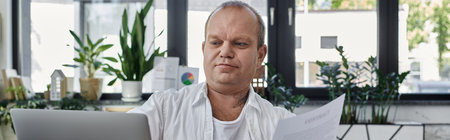 A man with inclusivity is working on his laptop in a modern office setting. He is surrounded by...