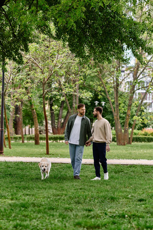 A bearded gay couple walks hand-in-hand through a verdant park with their labrador retriever.の写真素材