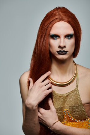 A drag performer with long red hair, blue eyeshadow, and a golden necklace and top poses for a photo shoot.の写真素材