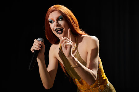 A drag performer in a gold dress and vibrant makeup holds a microphone on stage.